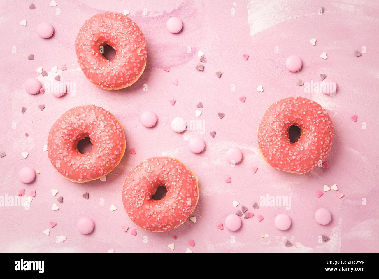 Donuts with pink icing and pink chocolate beans on pink background Stock Photo