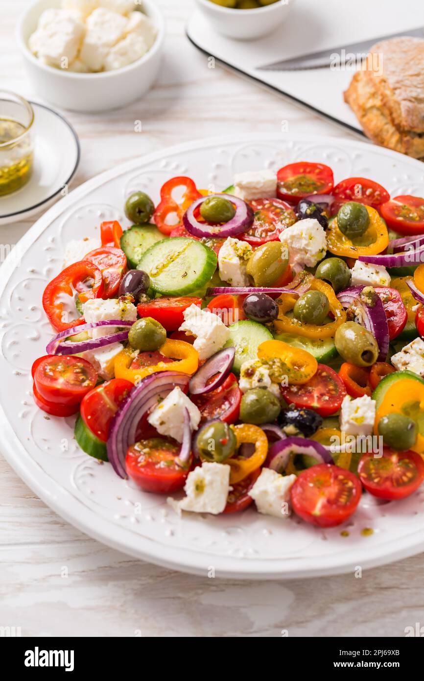 Greek salad of fresh cucumber, tomato, sweet pepper, lettuce, red onion, feta cheese and olives with olive oil dressing. Healthy food Stock Photo