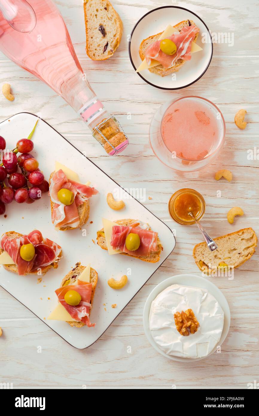 Flat lay of Appetizers and open sandwiches with Italian antipasti, camembert, Parma ham and rose wine on wooden table Stock Photo