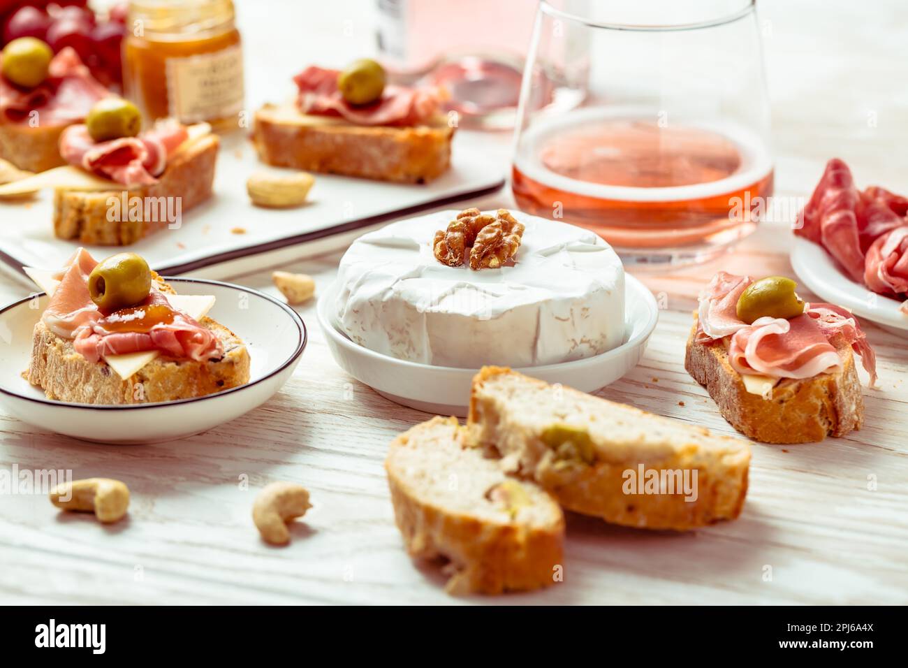 Appetizers and open sandwiches with Italian antipasti, camembert, Parma ham and rose wine on wooden table Stock Photo