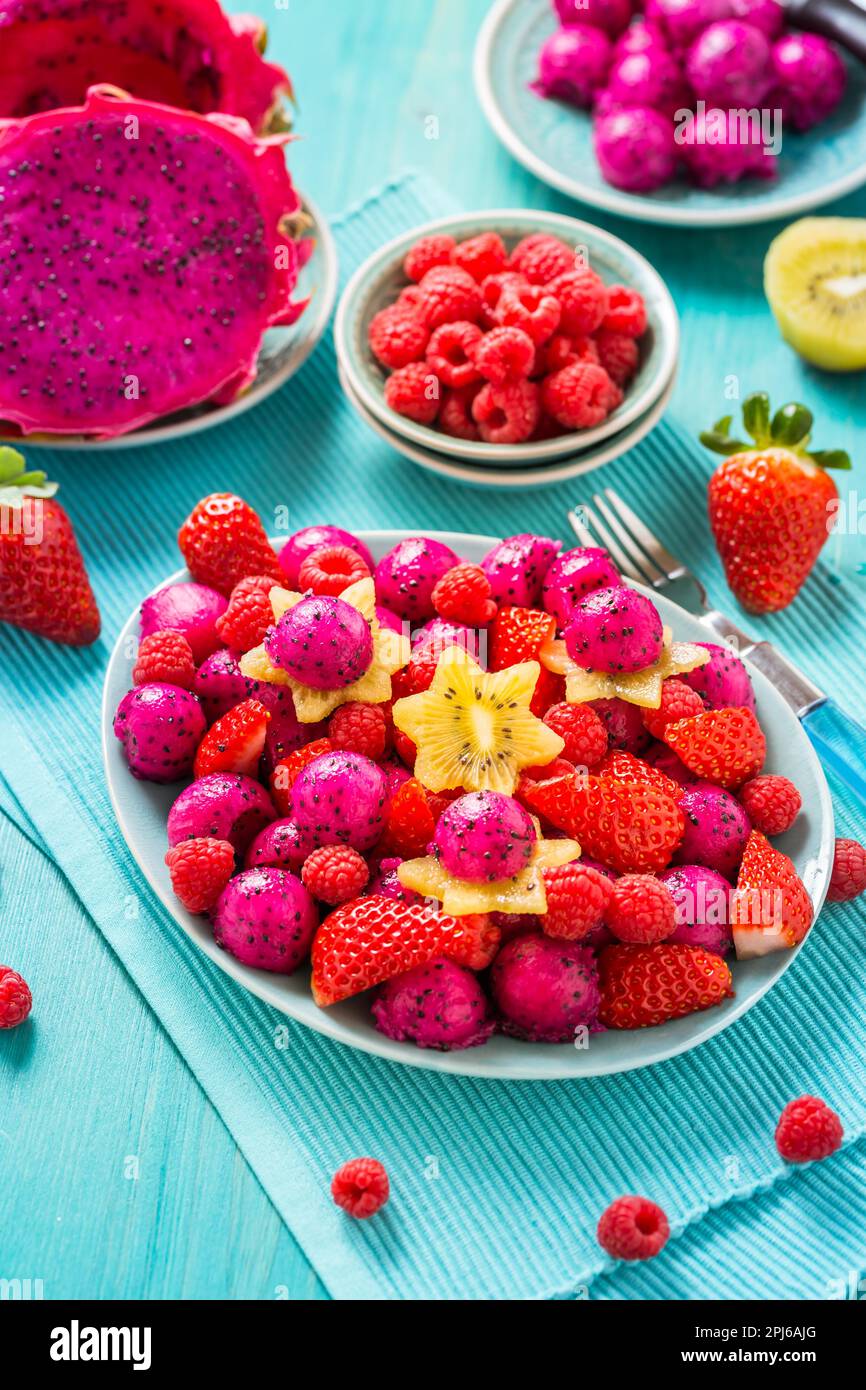 Fresh dragon fruit salad with strawberries, rspberries and start fruit (carambola) on cyan background Stock Photo