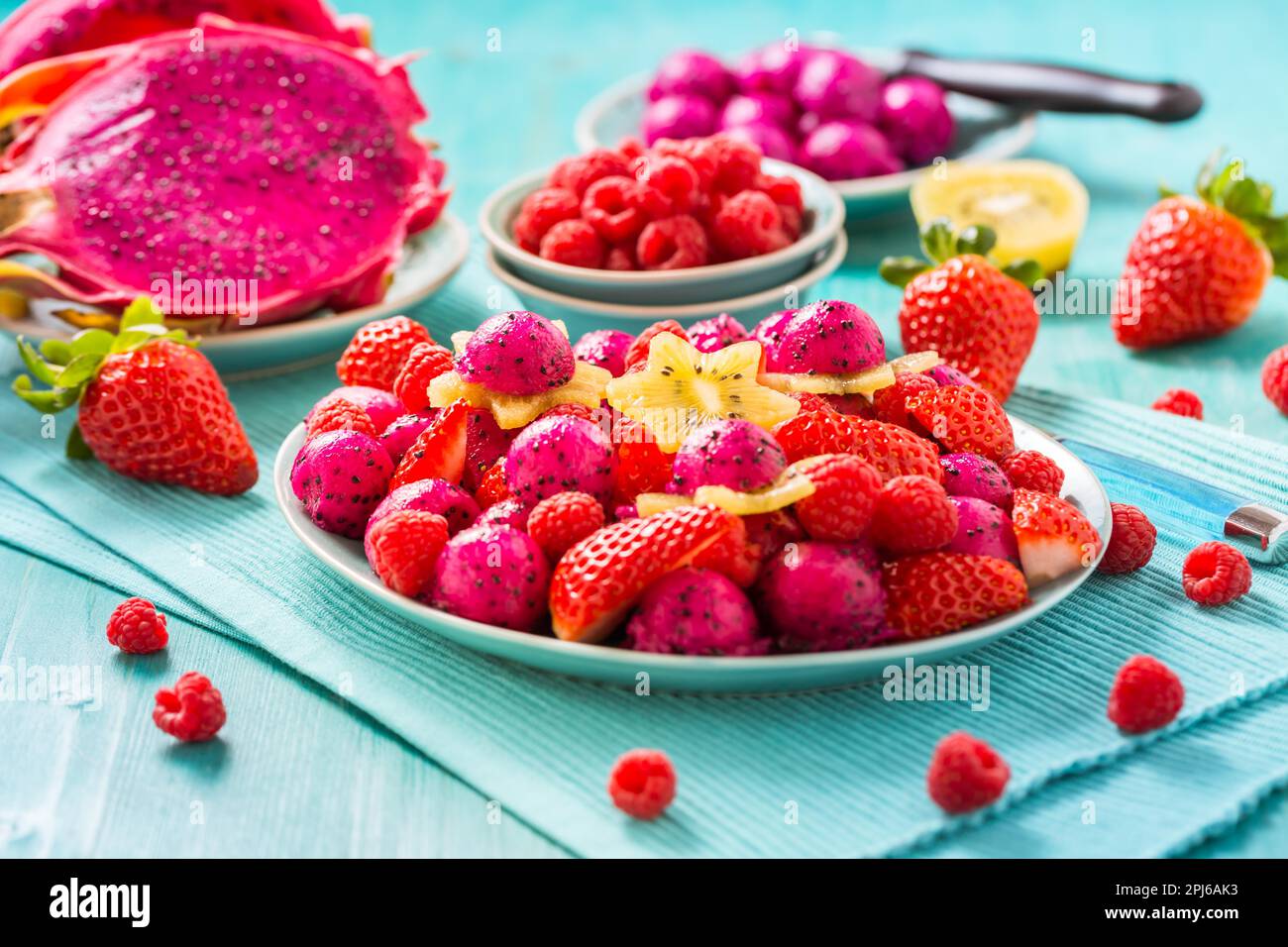 Fresh dragon fruit salad with strawberries, rspberries and start fruit (carambola) on cyan background Stock Photo