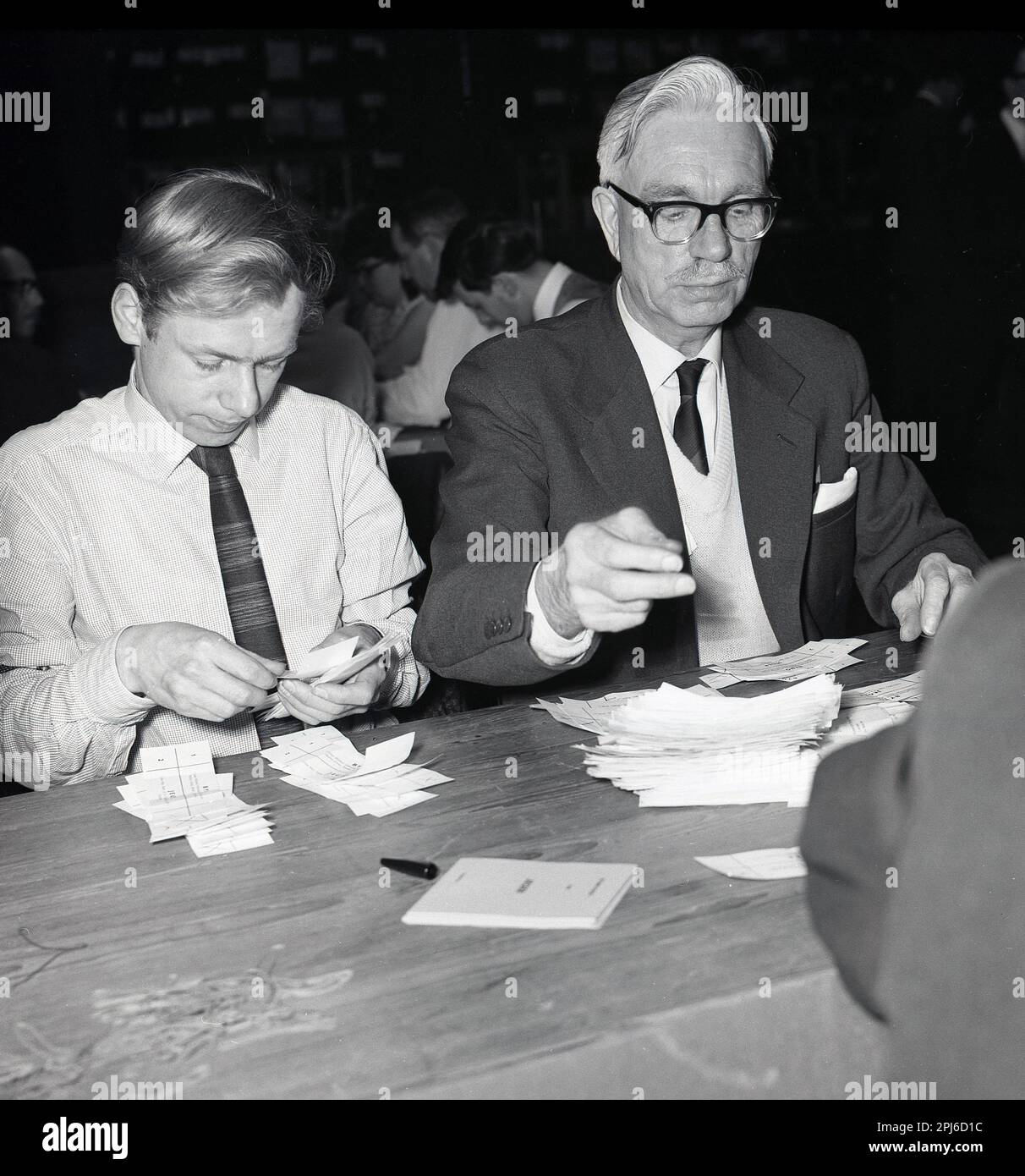 1960s, historical, two males, one elder, the other younger, sitting counting votes by hand at the St Pancras North constituency at the 1964 General election, London, England, UK. St Pancras North was created in 1885 and  elected a Member of Parliament up to 1983, when the area became part of a new constituency, Holborn and St Pancras. Stock Photo