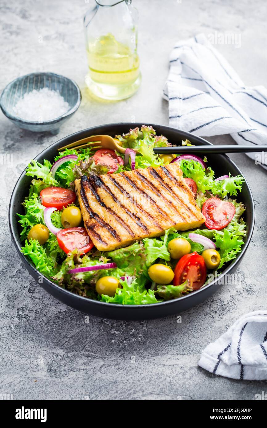 Fresh salad with grilled cheese, tomatoes and olives on grey Stock Photo