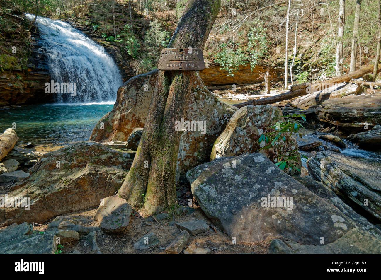 An old sign on a tree saying Stinging fork falls end of trail where it ends with the waterfall spilling in a turquoise color pool in the background an Stock Photo
