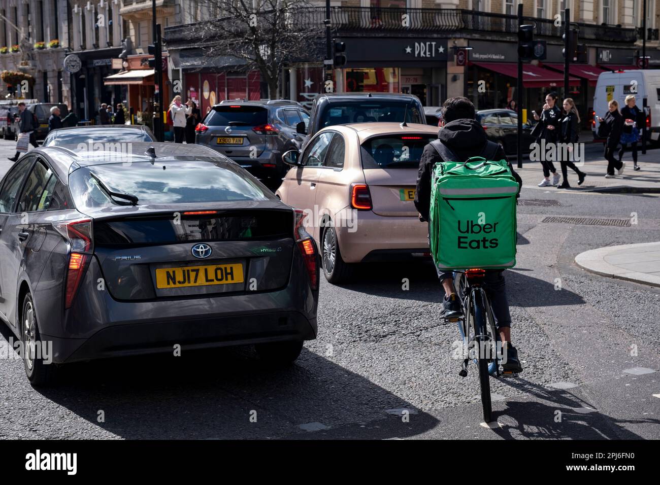 Uber Eats takeaway delivery cycle courier negotiating traffic on 27th March 2023 in London, United Kingdom. Uber Eats is an online food ordering and delivery platform launched by Uber in 2014. It acts as an intermediary between independent takeaway food outlets and customers, with thousands of cycle couriers delivering food by bicycle and other forms of transport. Gig workers are independent contractors, online platform workers, contract firm workers, on-call workers and temporary workers. Gig workers enter into formal agreements with on-demand companies to provide services to the companys cli Stock Photo