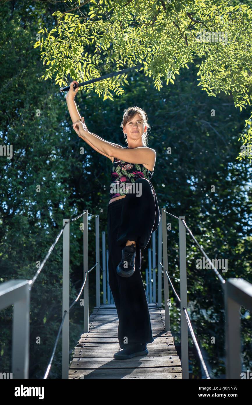 Woman practices tai chi sword on a bridge. The tai chi sword is an important instrument in this practice, as it is used to enhance concentration and p Stock Photo