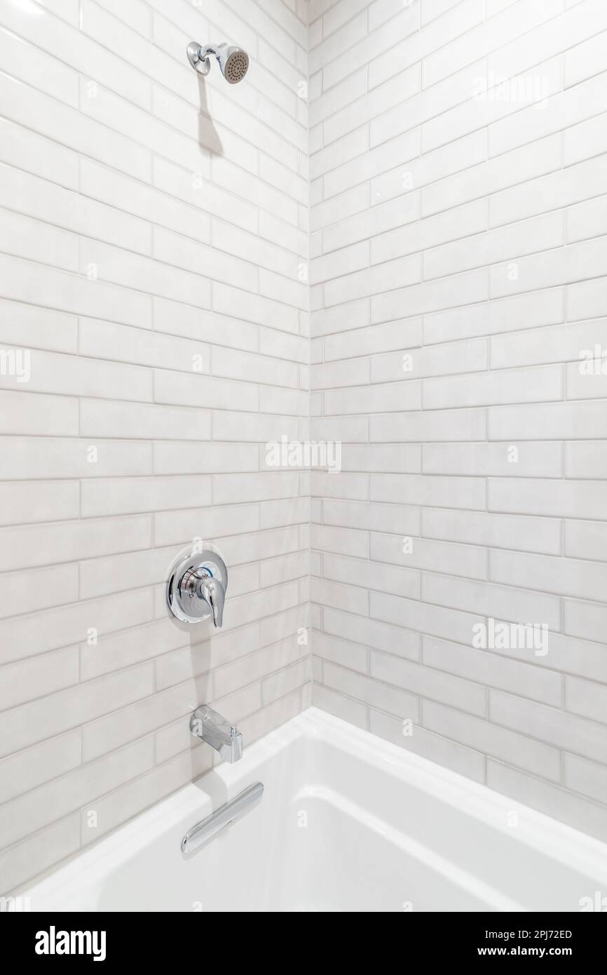 A shower and bathtub with tan subway tiles, white bathtub, and a chrome