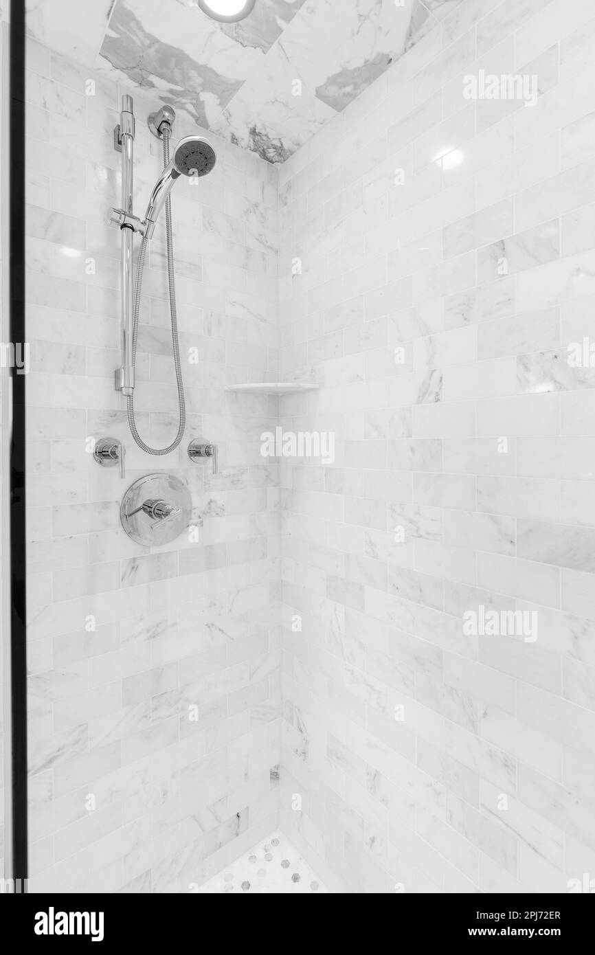 A walkin shower with marble subway tiles and a chrome faucet Stock