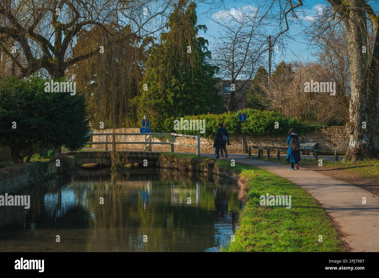 People walk along River Eye in Lower Slaughter in Cotswolds England on sunny day Stock Photo