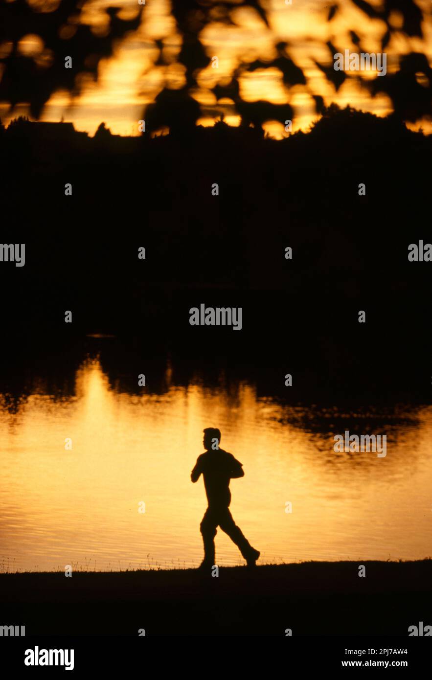 A silhouette of a man jogging alone a leak at sunset Stock Photo