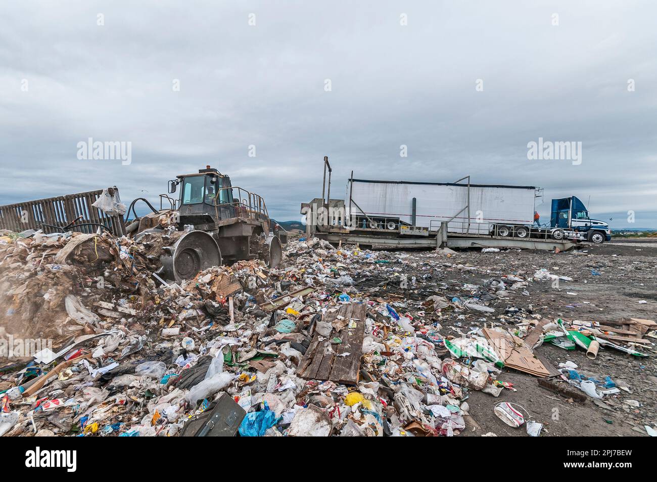 A soil compactor bulldozer pushing solid waste at an active landfill