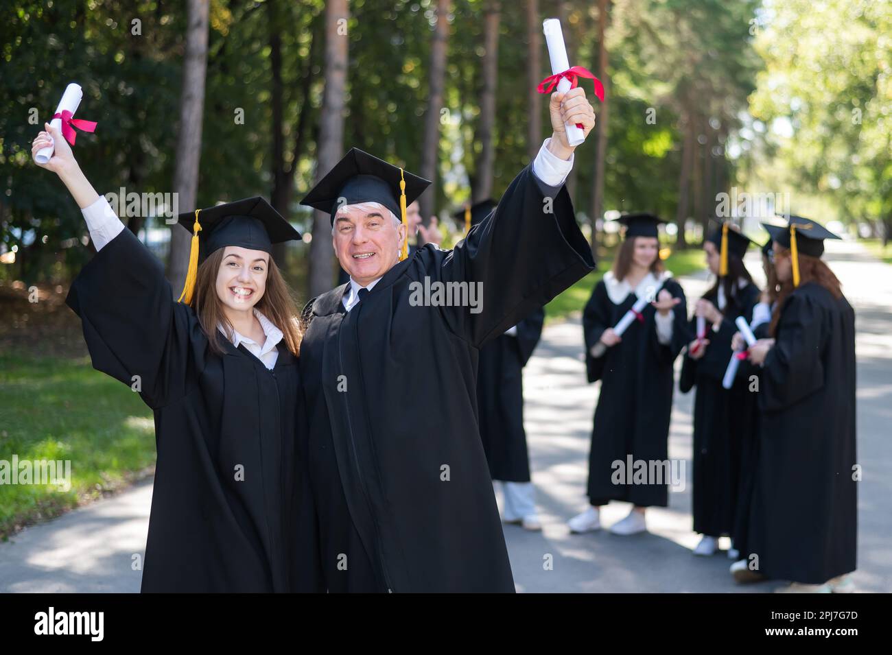 A group of graduates in robes outdoors. An elderly man and a young
