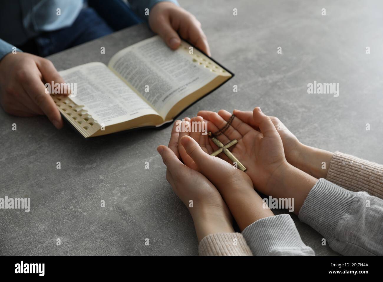 Boy praying and reading Bible with his godparents at grey table, closeup Stock Photo