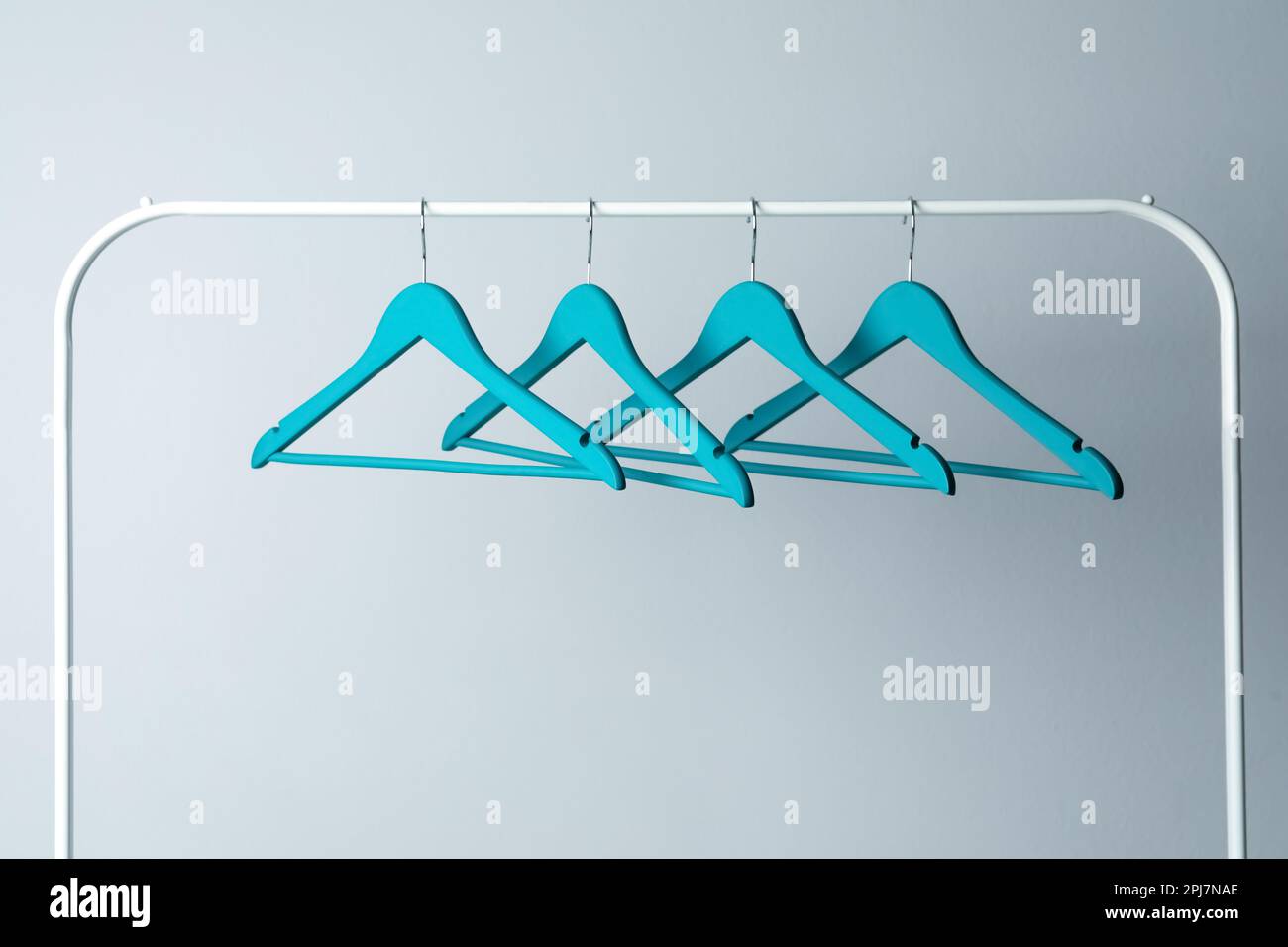 Empty turquoise clothes hangers on metal rack against light grey ...