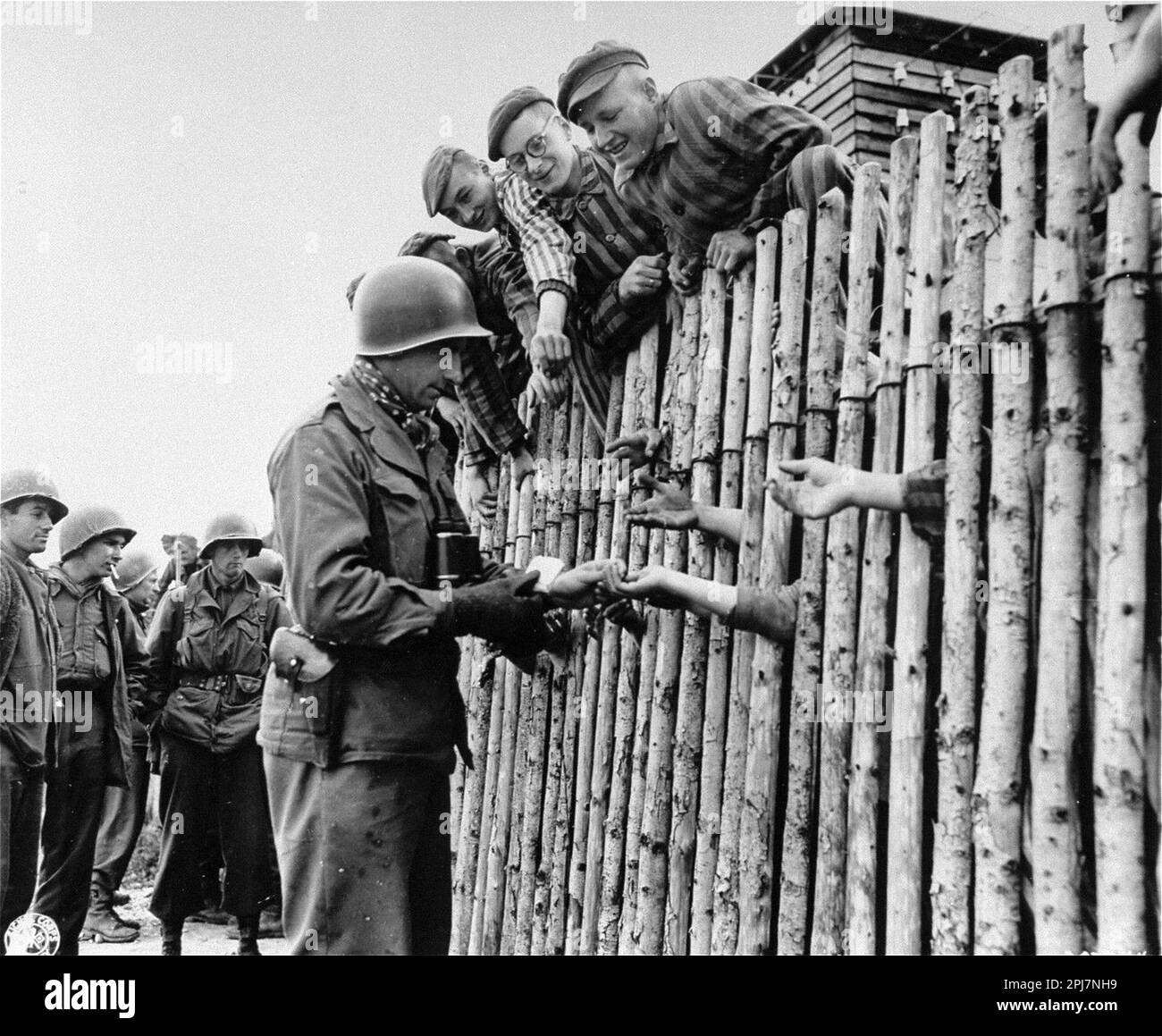 U.S. Army Corporal Larry Matinsk puts cigarettes into the extended hands of newly liberated prisoners behind a stockade in the Allach concentration camp, near Dachau Germany on April 30, 1945. Stock Photo
