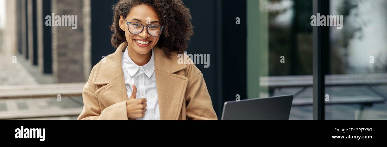 Smiling african business woman showing thumb up while working laptop ...