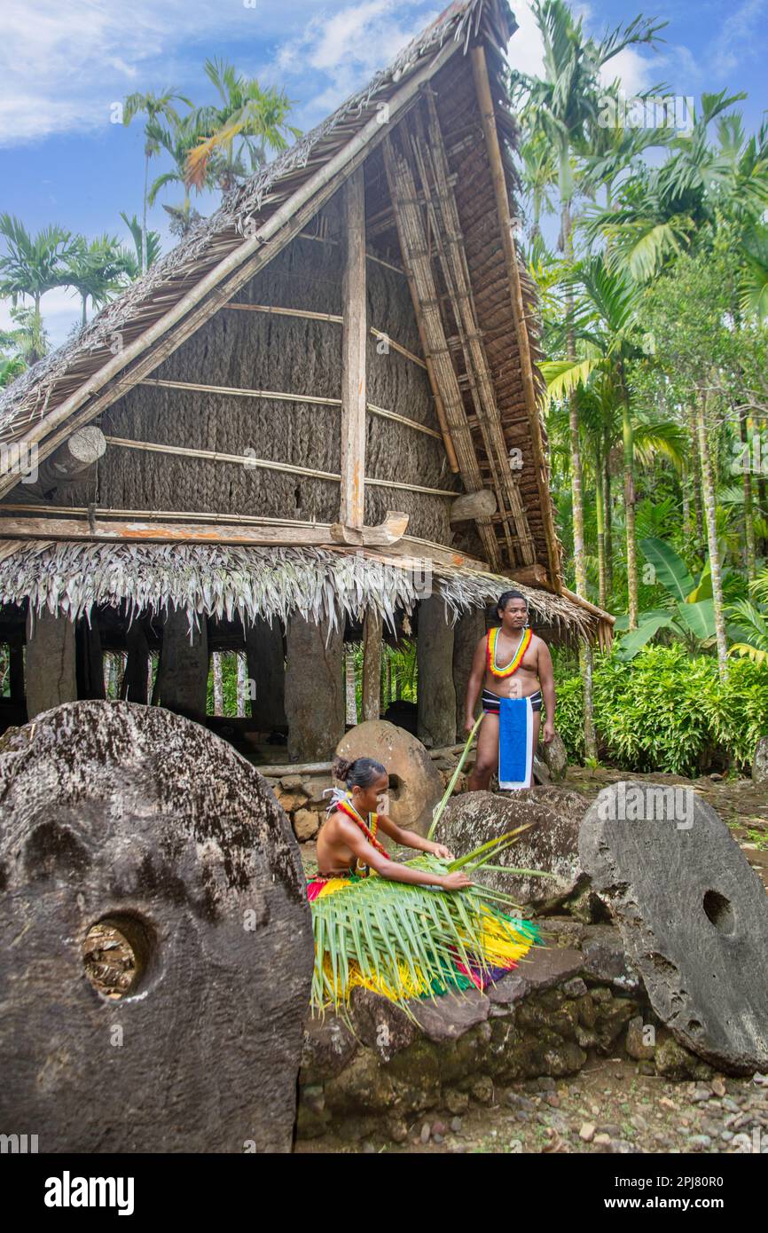 This couple (MR) are in traditional outfits for cultural cerimonies. The young woman is weaving a basket from a palm frond and surrounded by stone mon Stock Photo