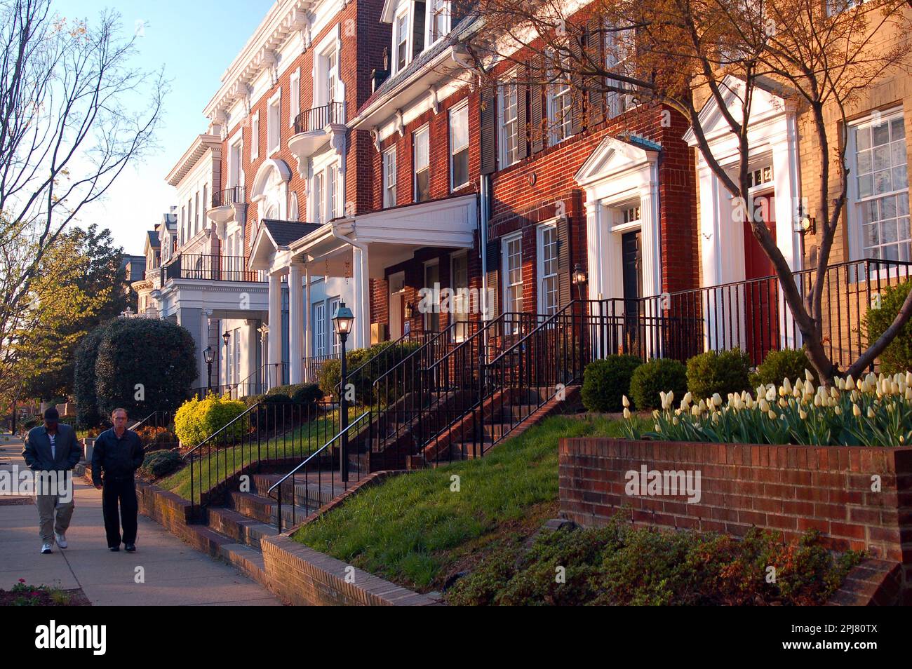Two adult men walk past the historic homes on Monument Avenue in