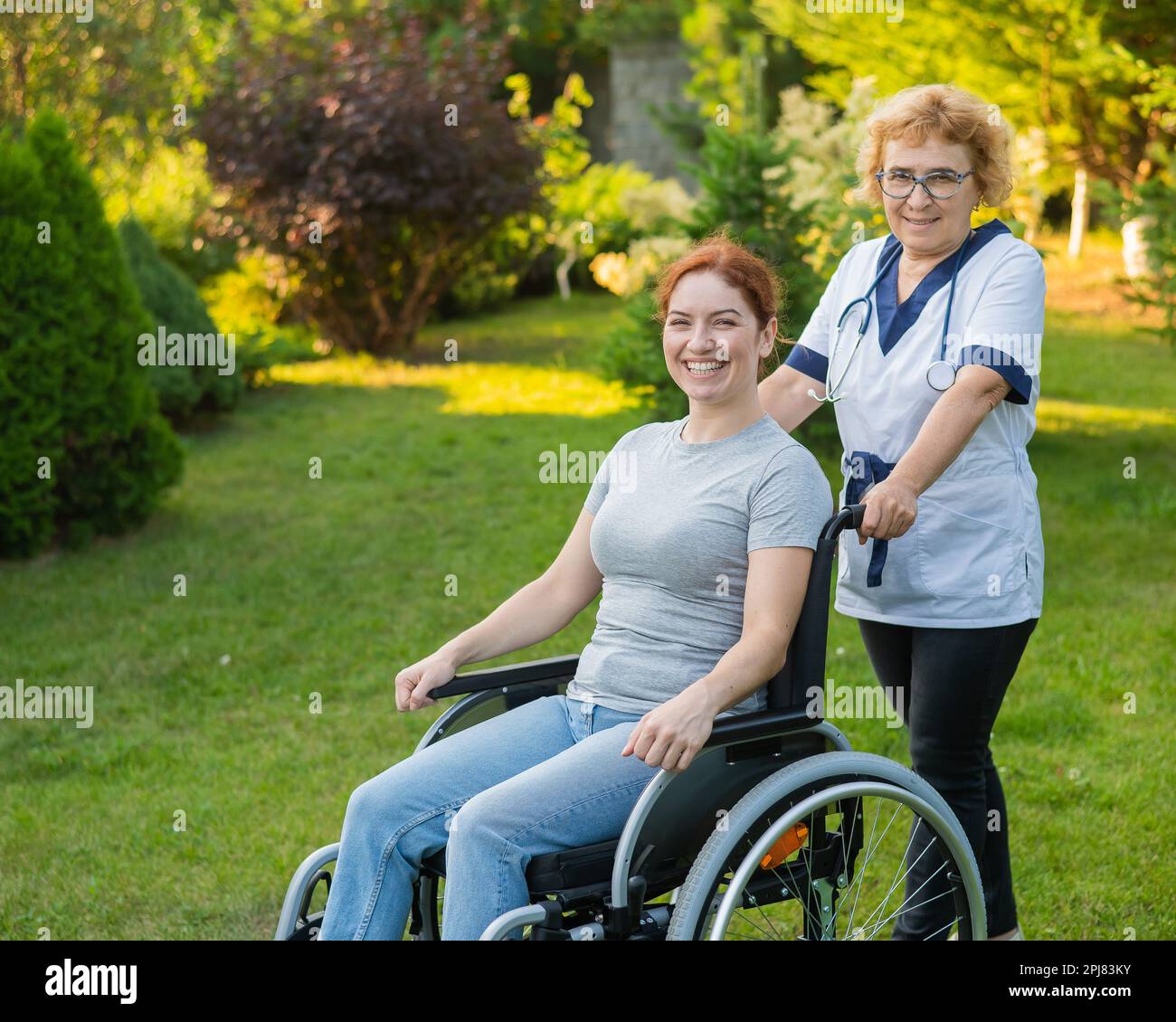 An elderly female nurse walks with a middle-aged woman in a wheelchair ...