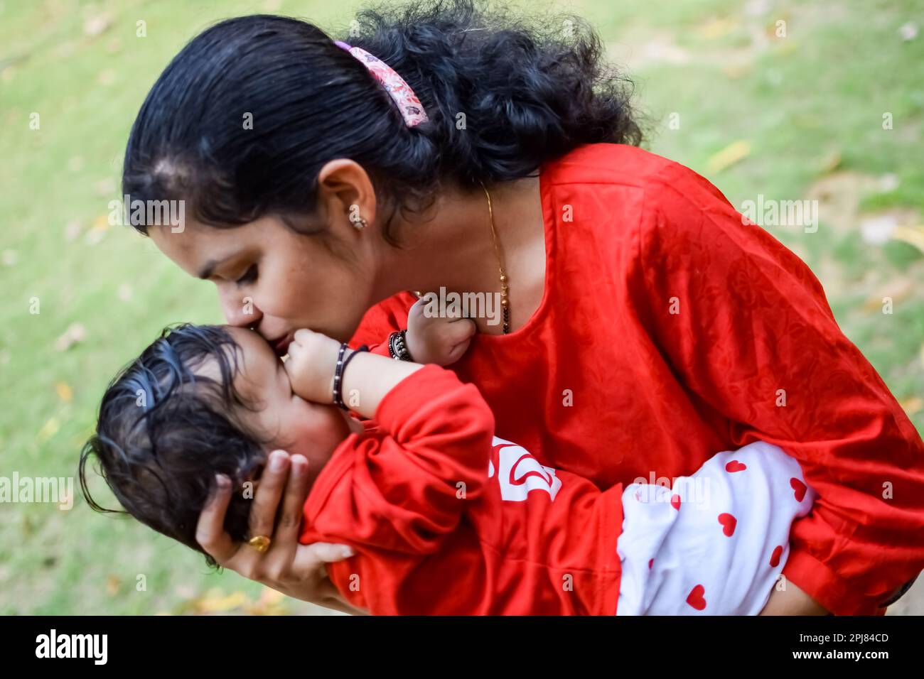 Loving mom carrying of her baby at society park. Bright portrait of happy mum holding child in her hands. Mother hugging her little 9 months old son. Stock Photo