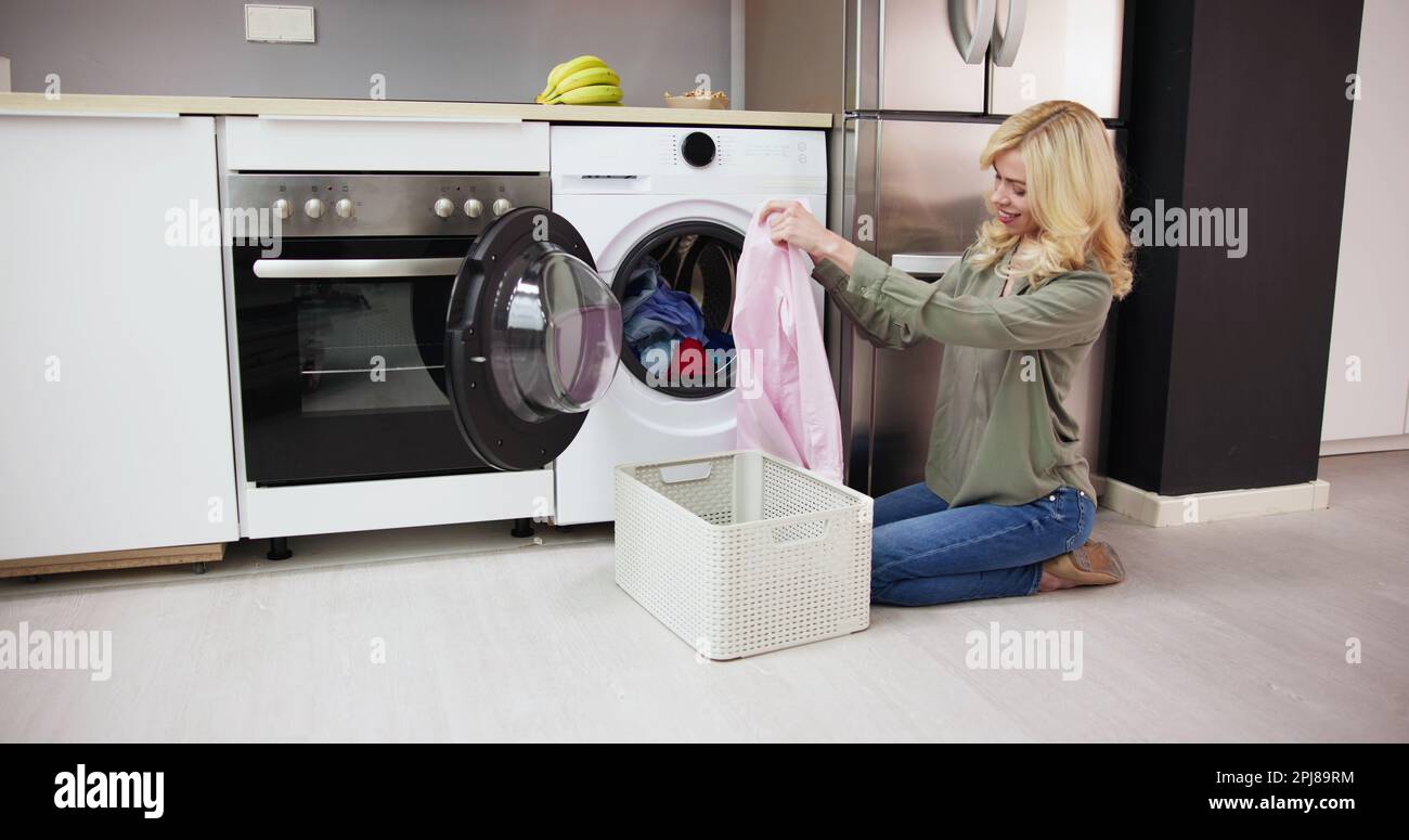 Woman Smelling Clean Clothes Near The Electronic Washer At Laundry Room Stock Photo