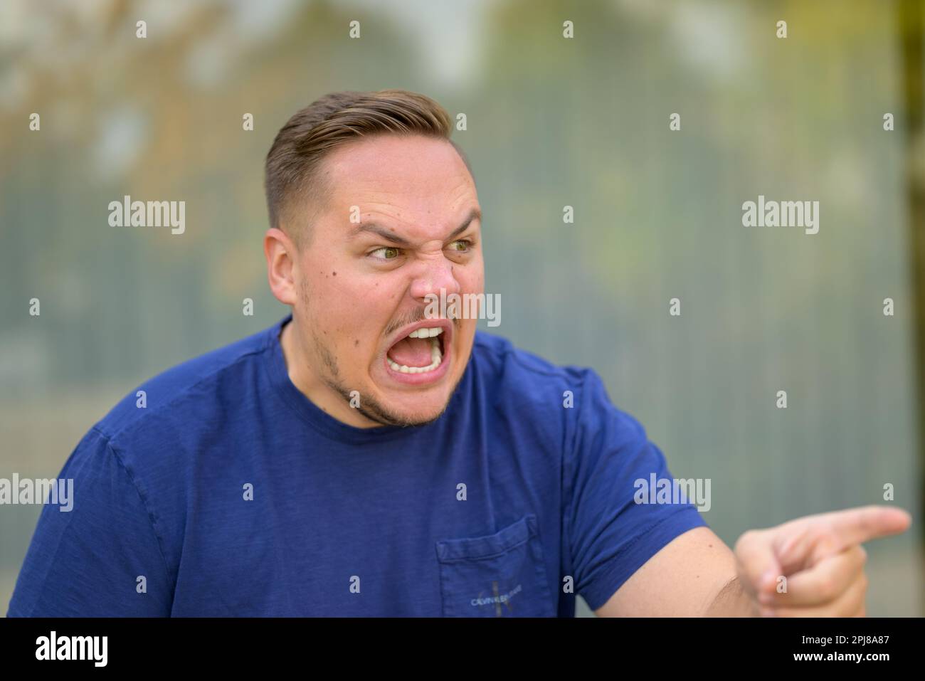 Extremely angry aggressive young man yelling and pointing at someone Stock Photo