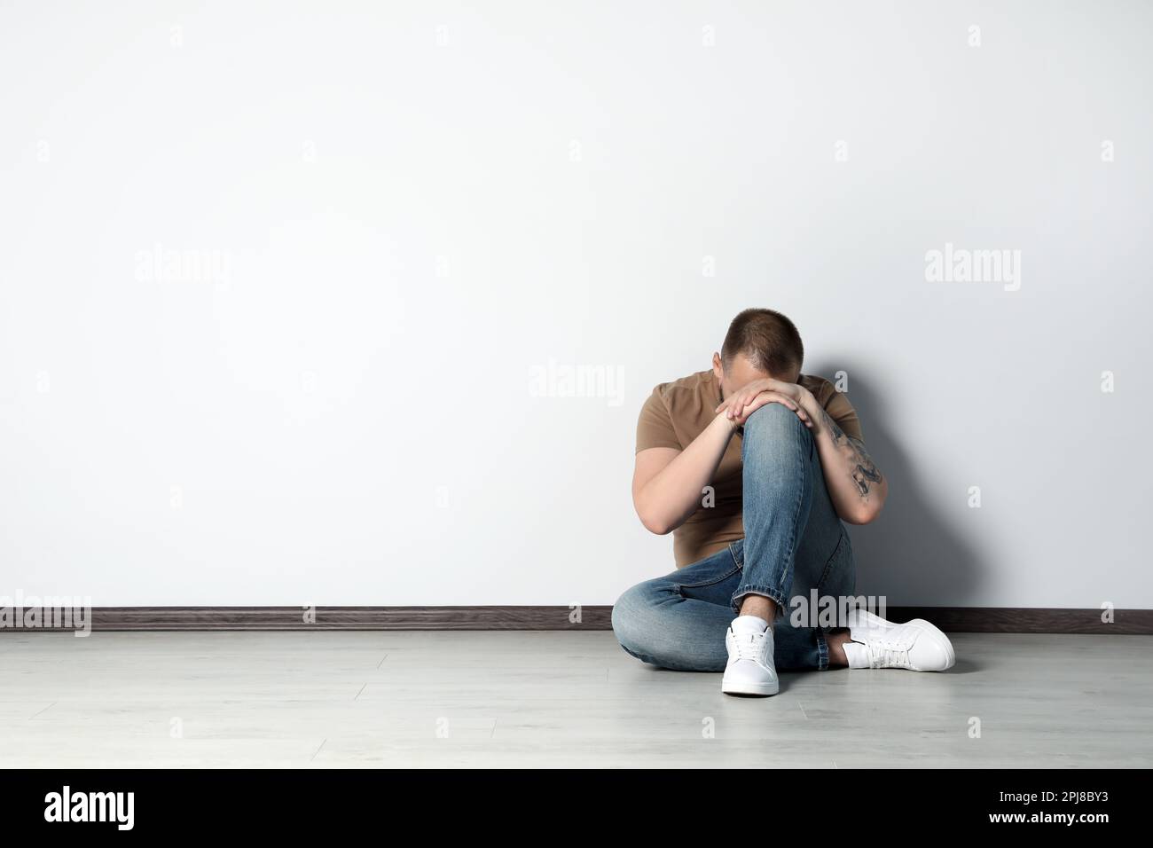 Sad young man sitting on floor near white wall indoors, space for text Stock Photo