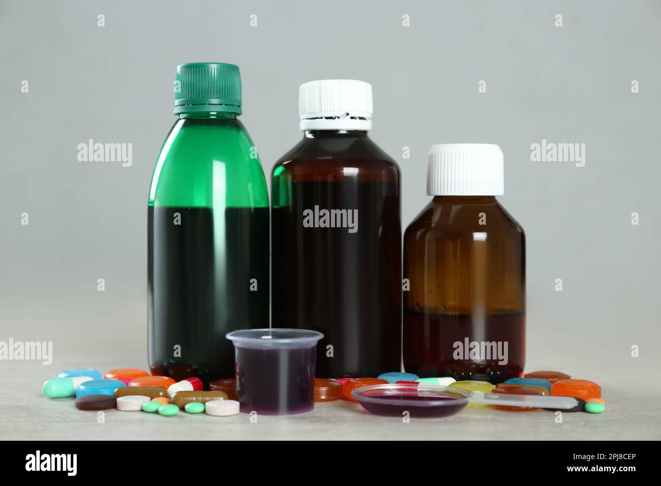 Bottles of cough syrup, dosing spoon, measuring cup and pills on light ...