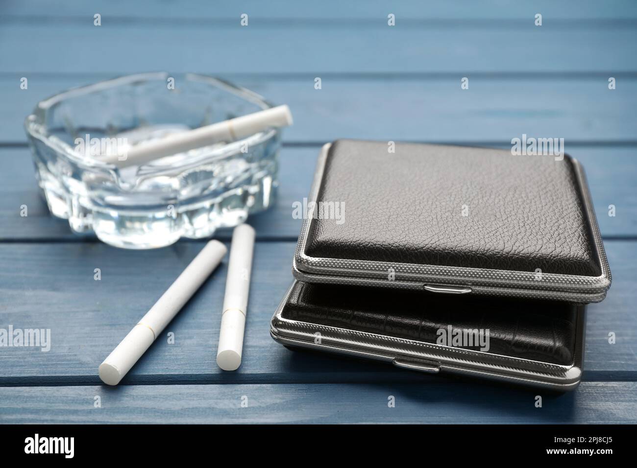 Closed leather cigarette cases with ashtray on blue wooden table, closeup  Stock Photo