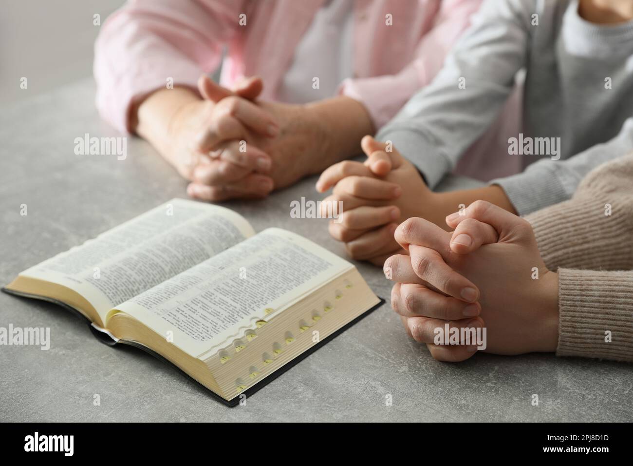 Boy and his godparents praying together at grey table, closeup Stock Photo