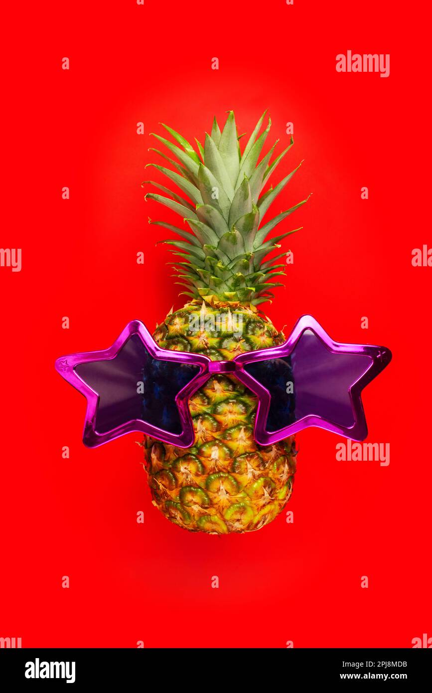 Pineapple with sunglasses on red background. Pineapple in star glasses. Stock Photo