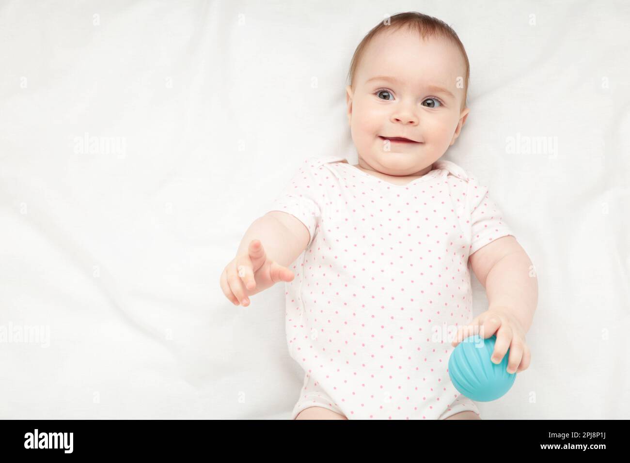 Cute baby girl playing with sensory ball on bed. Top view Stock Photo