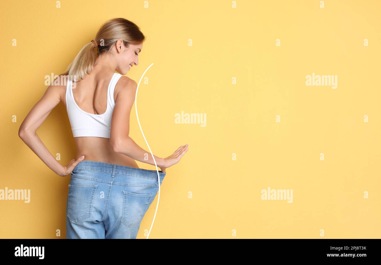 Happy young woman with slim body in oversized jeans on yellow background, space for text. Weight loss Stock Photo