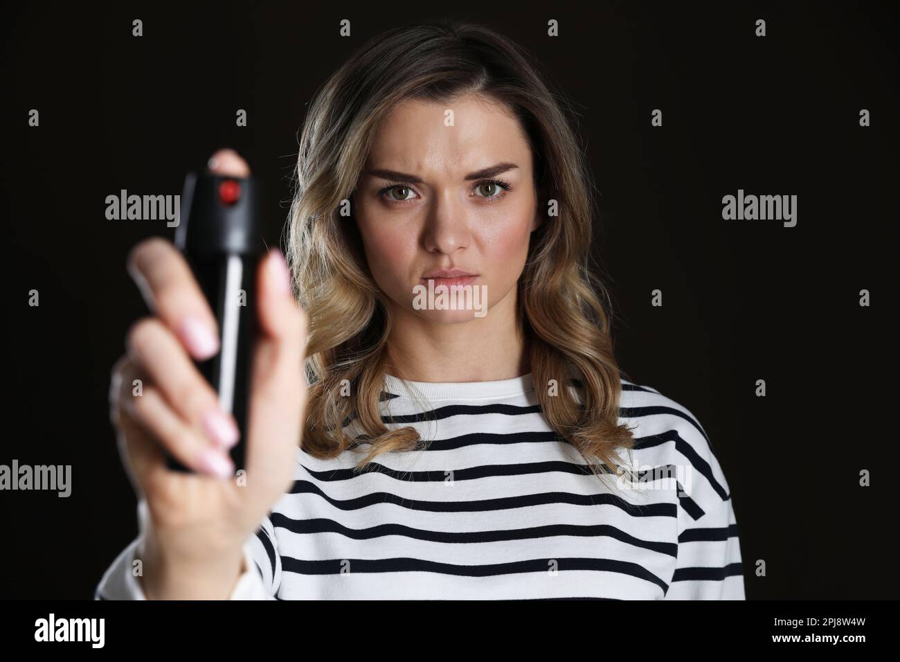 Young woman using pepper spray on black background Stock Photo - Alamy