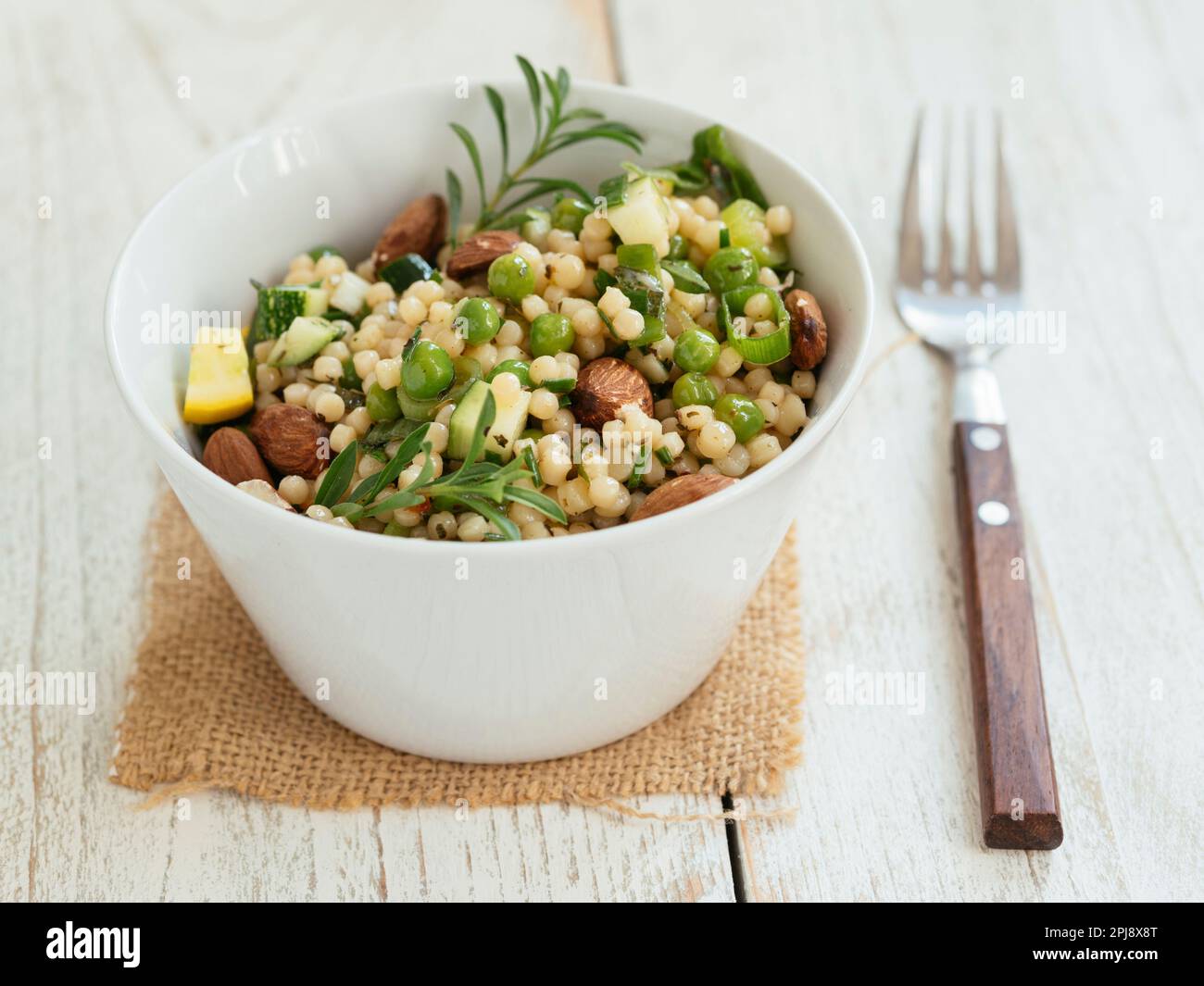 Bowl with a pearl couscous salad with peas, zucchini and almonds. Stock Photo