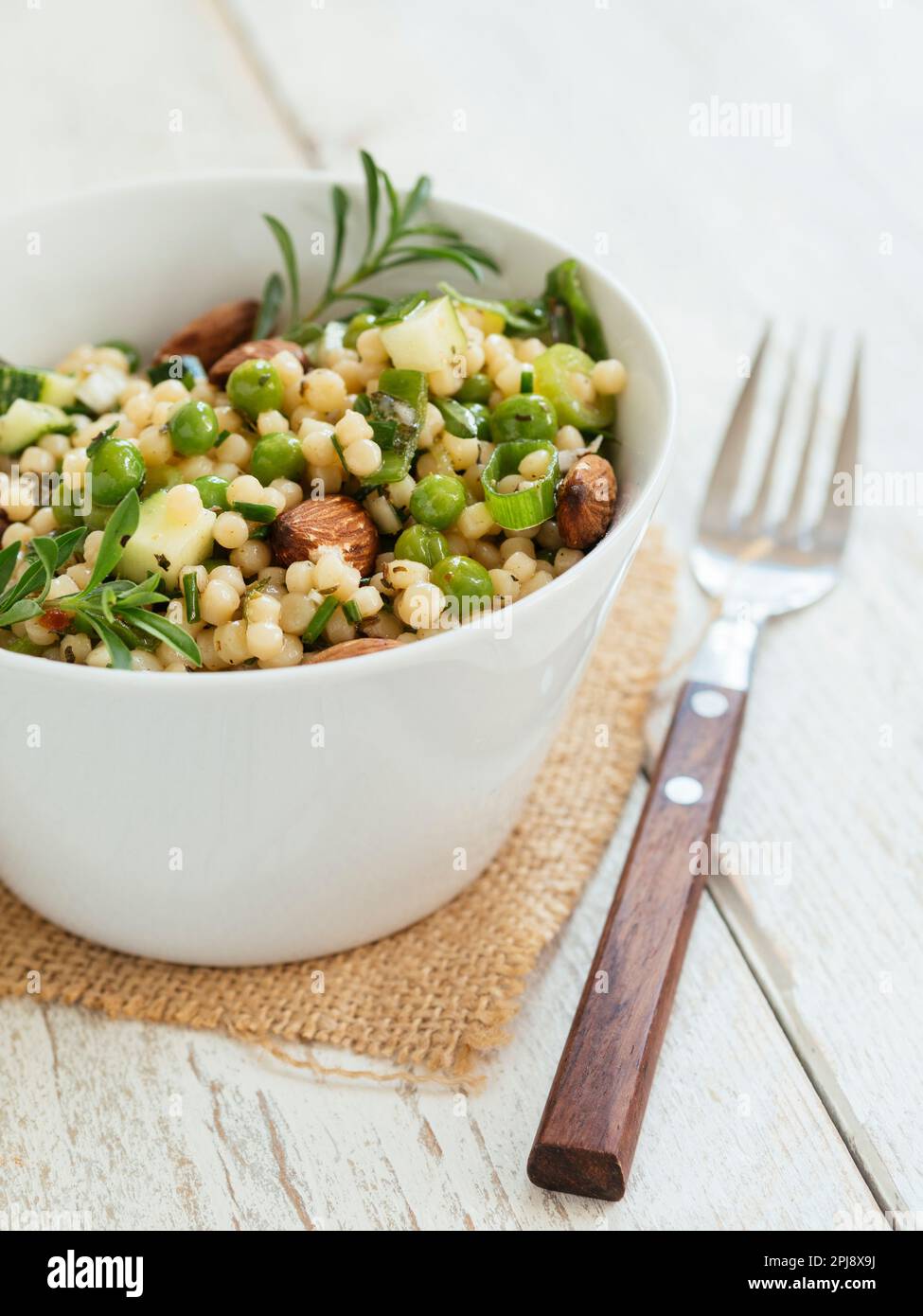 Bowl with a pearl couscous salad with peas, zucchini and almonds. Stock Photo