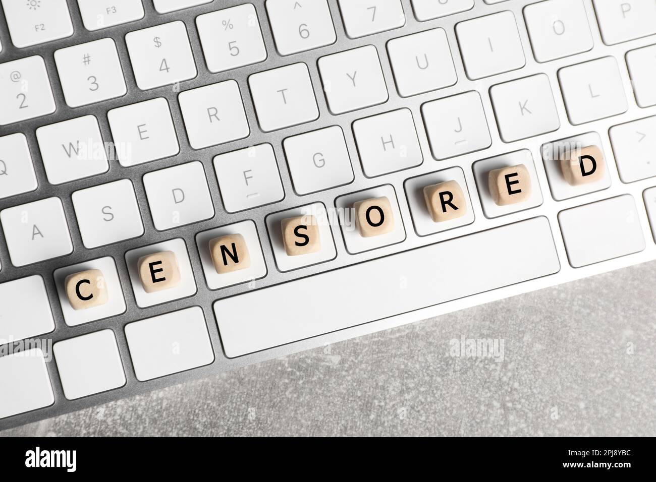 Wooden cubes with word Censored and keyboard on light grey table, top ...