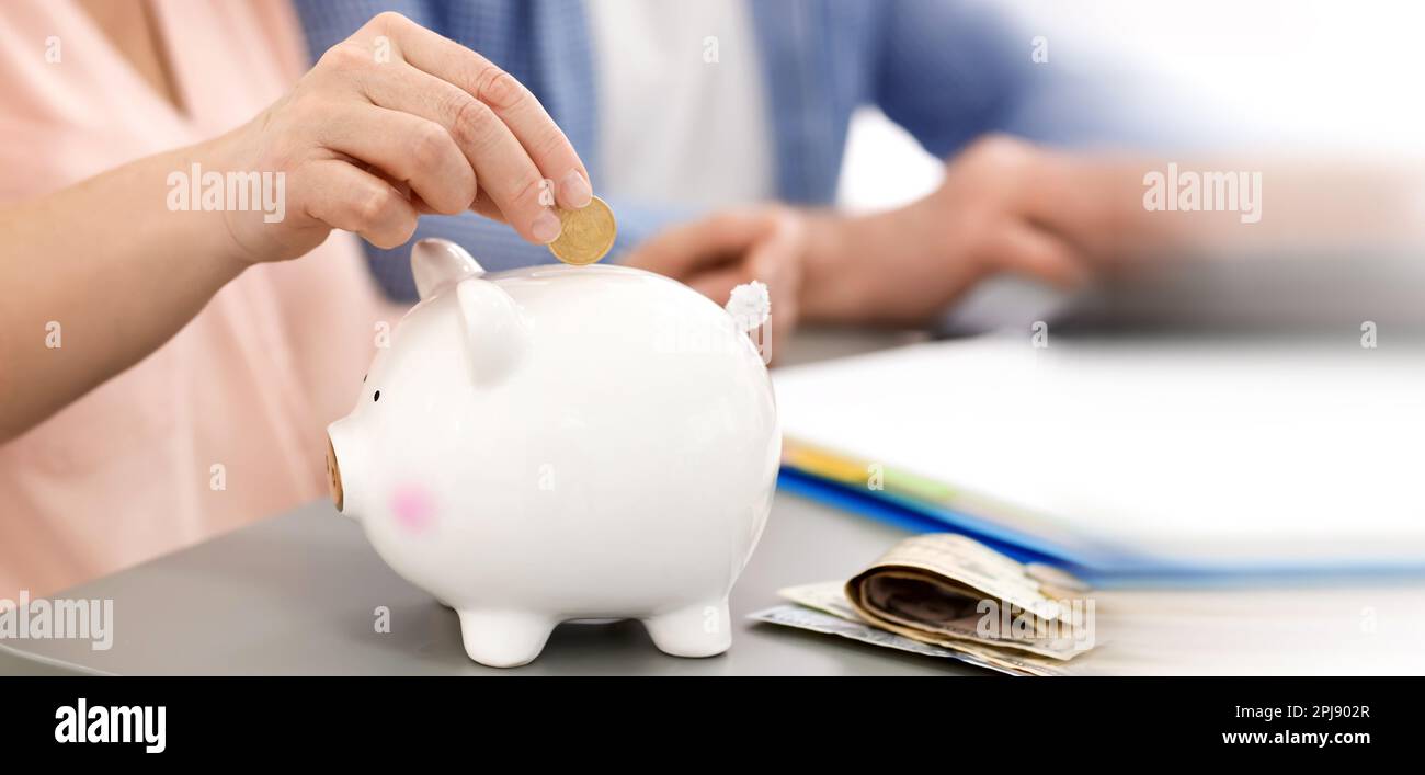 Mature woman putting coin in piggy bank at table, closeup. Banner ...