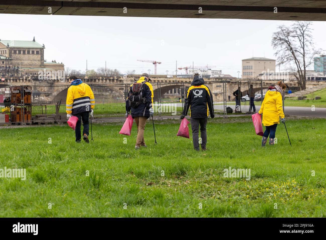 Dresden, Germany. 01st Apr, 2023. Four employees of Deutsche Post AG walk on the meadow with the red bags of the city of Dresden for the Elbe meadow cleaning. The area of operation of the extends on both sides of the Elbe from Cossebaude to Pillnitz and is a total of 30 kilometers long. Credit: Daniel Schäfer/dpa/Alamy Live News Stock Photo