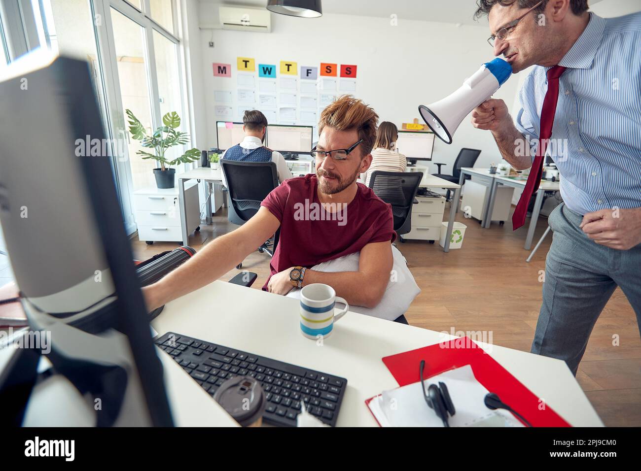 A manager is yelling on a sleepy employee through a megaphone at work in a uniform atmosphere in the office. Employees, job, office Stock Photo