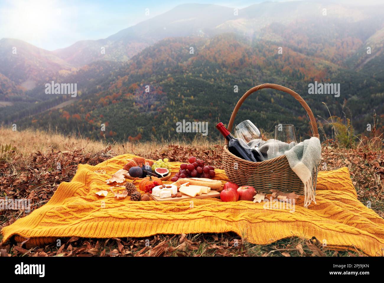 Knitted plaid with picnic basket, wine and snacks in mountains on ...