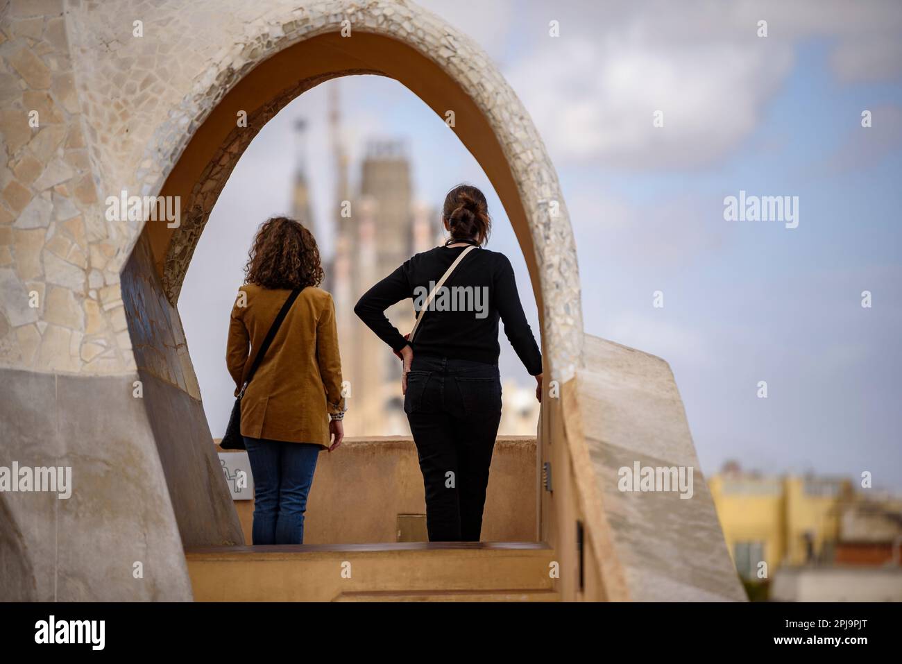 The Passion Facade of the Sagrada Família seen behind an arch of the Casa Milà - La Pedrera (Barcelona, Catalonia, Spain) Stock Photo