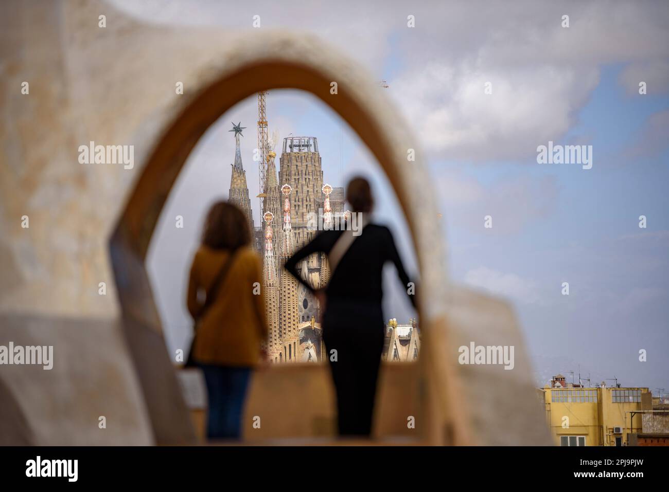 The Passion Facade of the Sagrada Família seen behind an arch of the Casa Milà - La Pedrera (Barcelona, Catalonia, Spain) Stock Photo