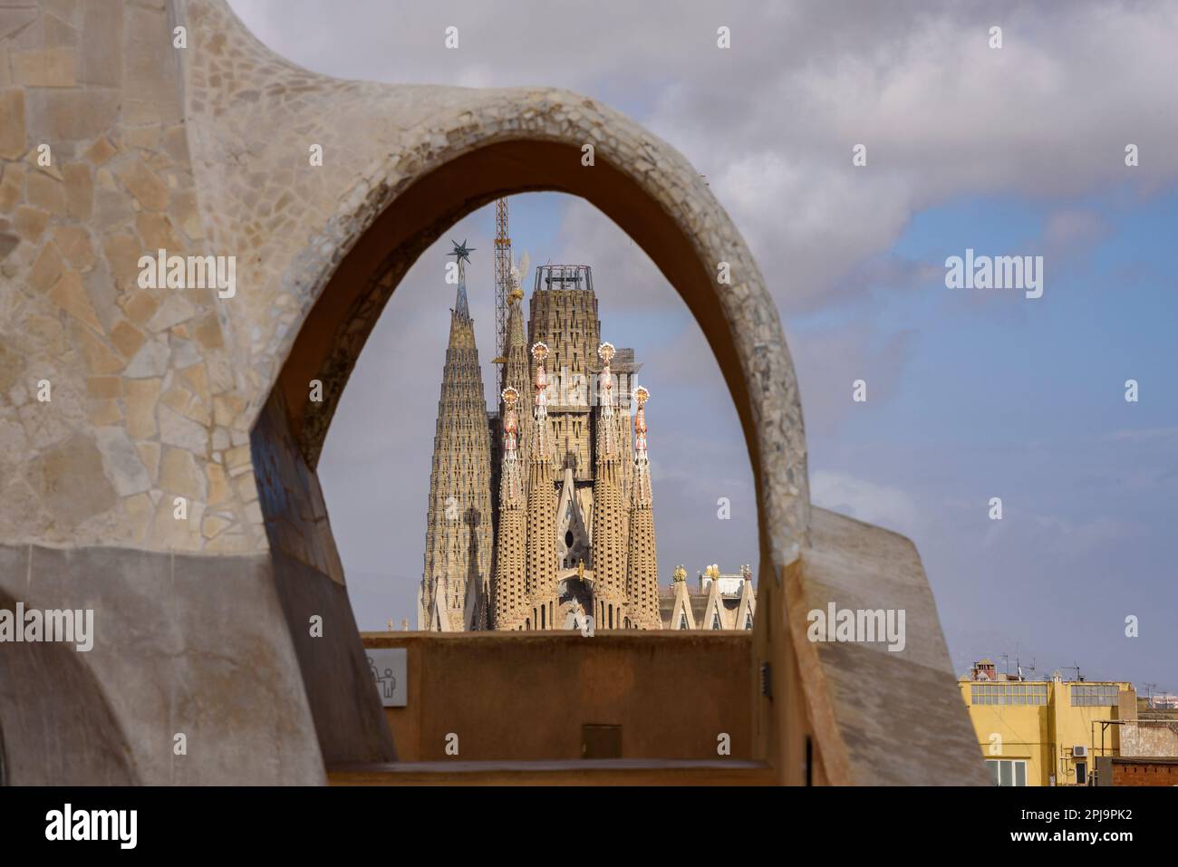 The Passion Facade of the Sagrada Família seen behind an arch of the Casa Milà - La Pedrera (Barcelona, Catalonia, Spain) Stock Photo