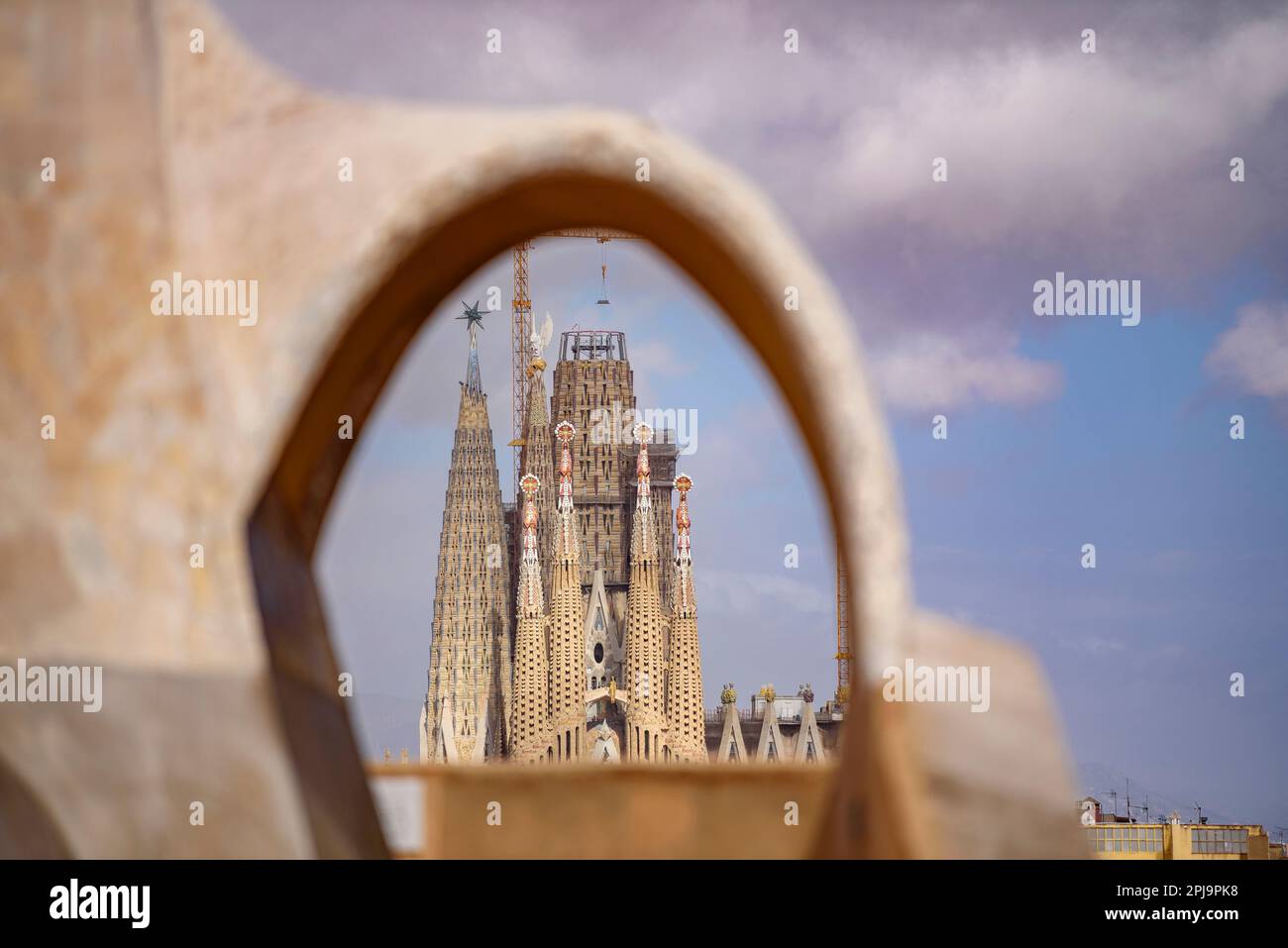 The Passion Facade of the Sagrada Família seen behind an arch of the Casa Milà - La Pedrera (Barcelona, Catalonia, Spain) Stock Photo