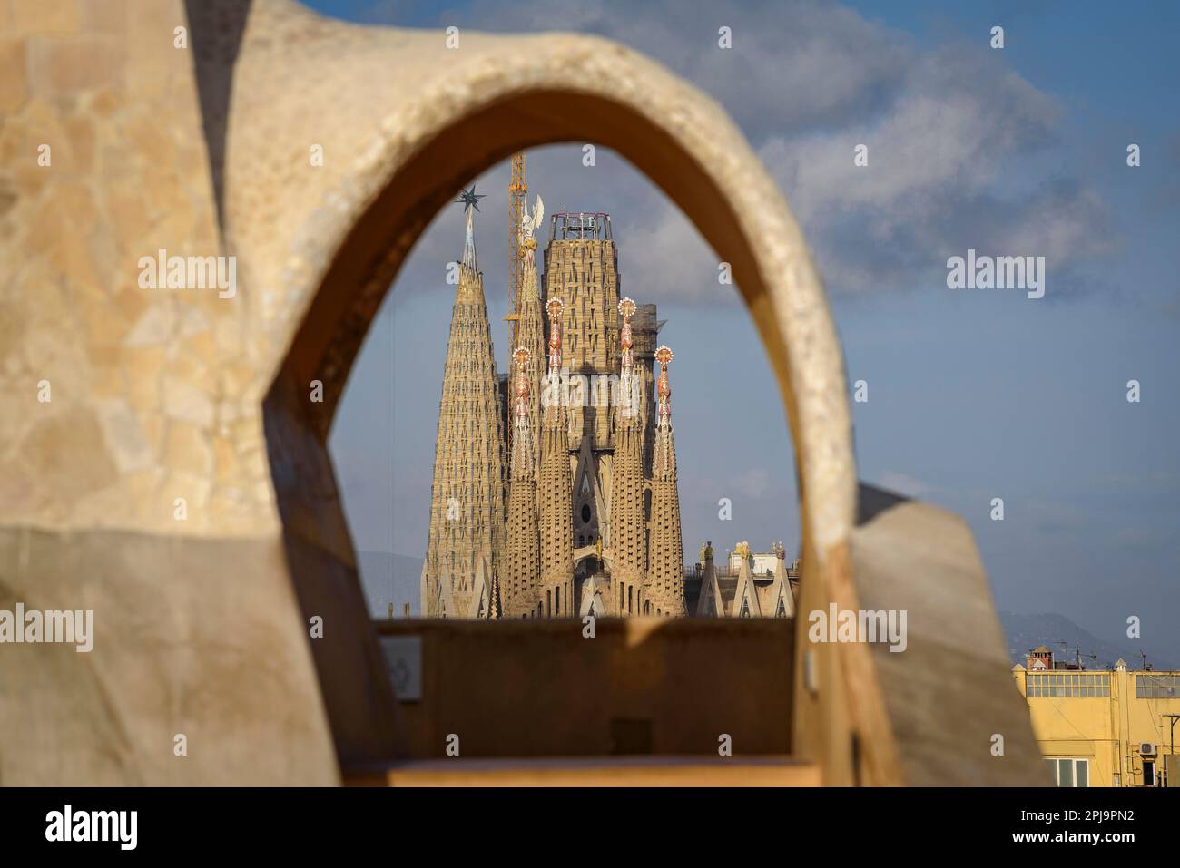 The Passion Facade of the Sagrada Família seen behind an arch of the Casa Milà - La Pedrera (Barcelona, Catalonia, Spain) Stock Photo