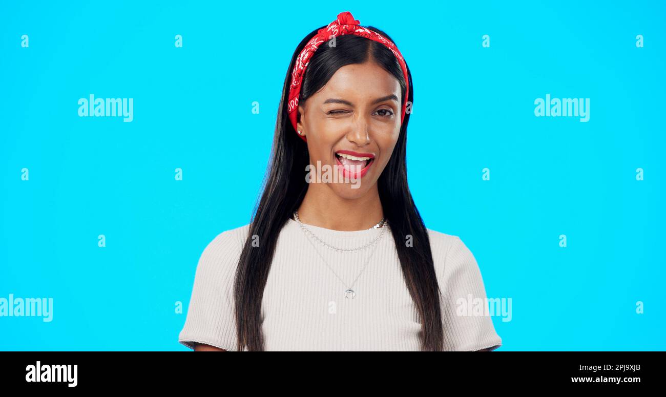 Happy woman, face and wink on blue background, laughing and flirting in studio. Portrait of