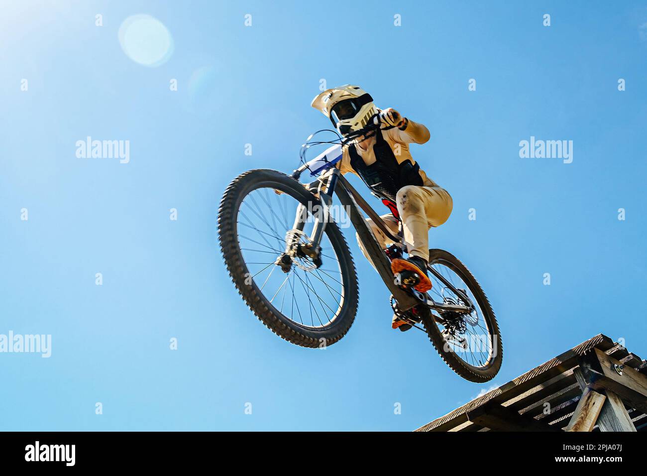 female rider on downhill bike jumping wooden drop, background blue sky, racing DH mountain bike, extreme sport games Stock Photo