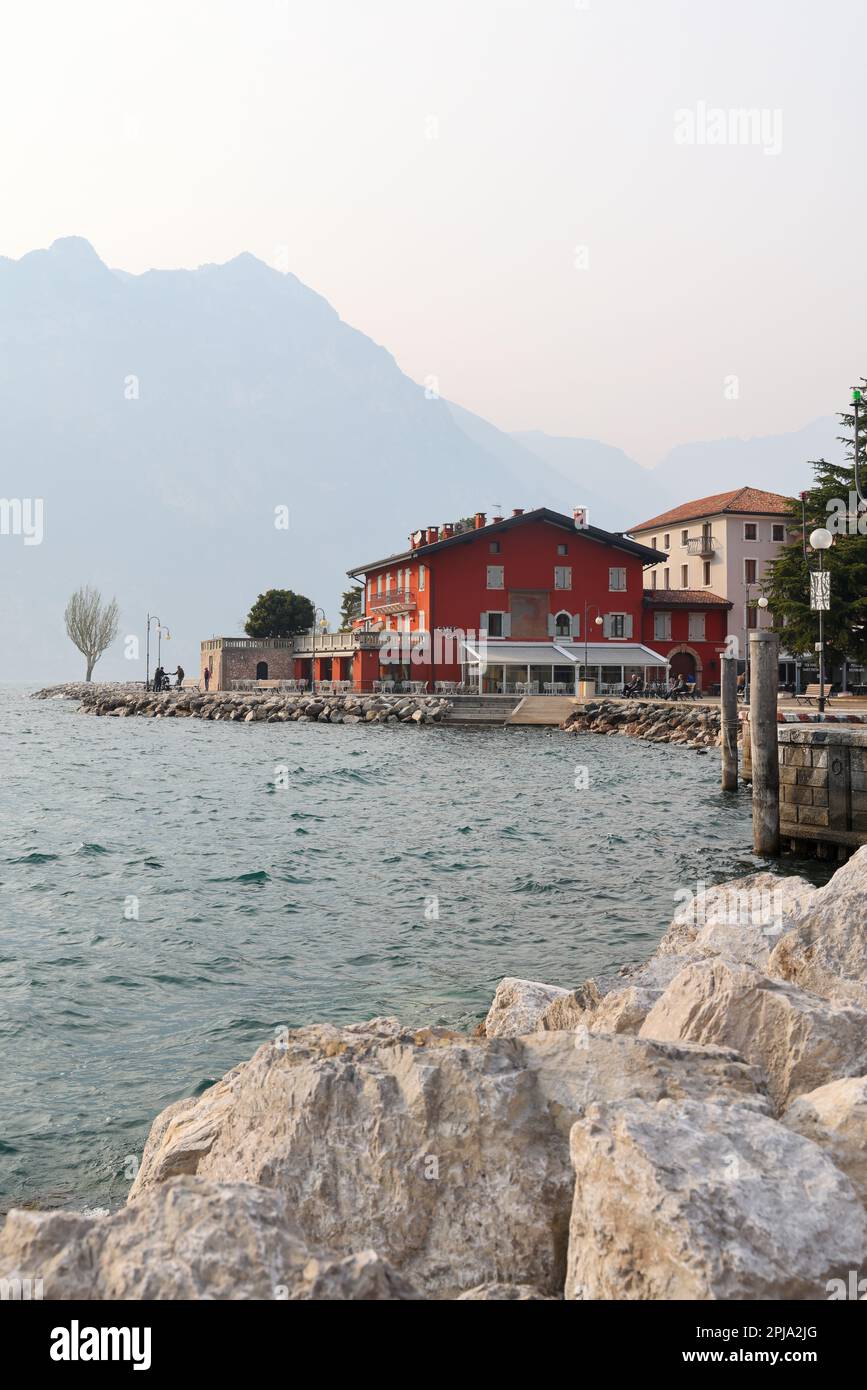 Spring landscape with stone pathway and colorful buildings and mountaind in mist, Lake Garda, Torbole town, Italy, Europe 03 20 2023 Stock Photo